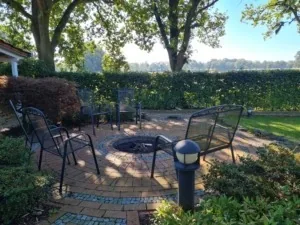 Gartenstühle rund um einen gepflasterten Feuerplatz unter Bäumen