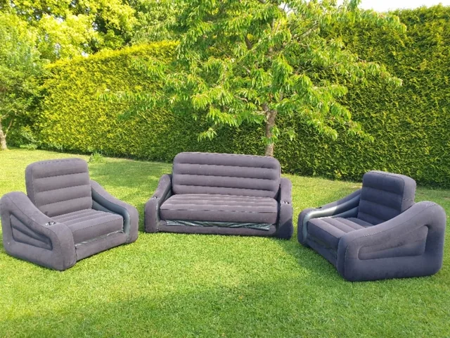 Graue aufblasbare Sessel und ein Sofa auf dem Rasen vor einer grünen Hecke