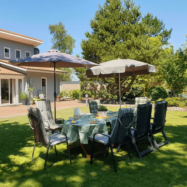 Gedeckter Gartentisch mit gepolsterten Stühlen unter zwei Sonnenschirmen