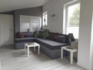 Heller Wohnbereich mit grauem Ecksofa und kleinen Beistelltischen